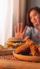 A woman making hand sign to refuse a hamburger, french fries and