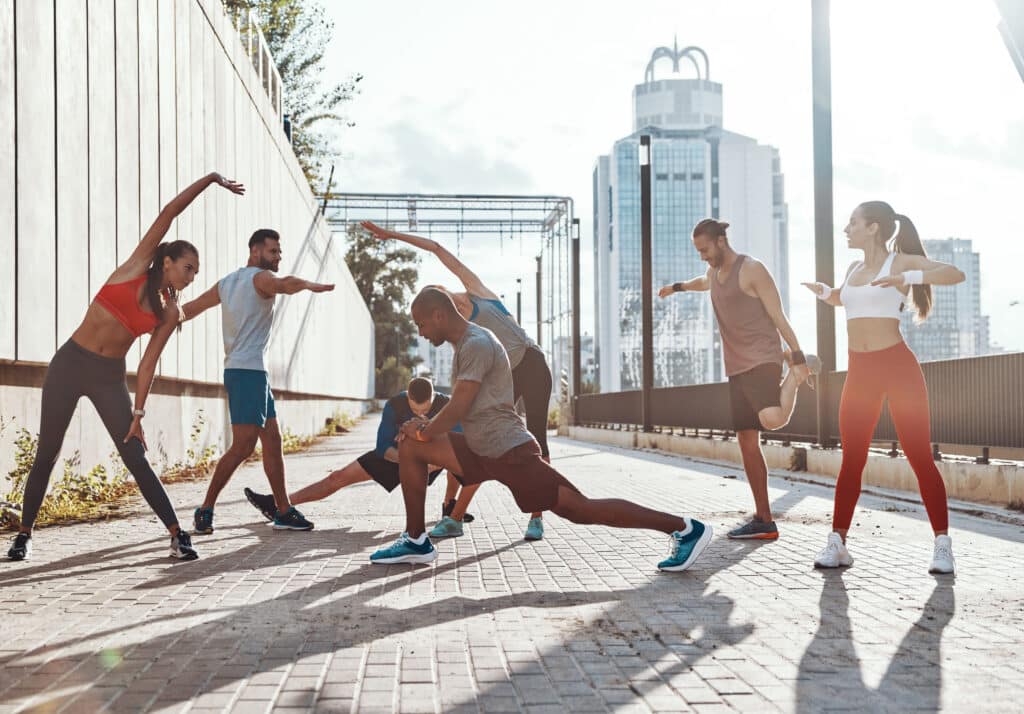 Full length of people in sports clothing warming up and stretching while exercising on the sidewalk outdoors