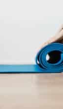 Crop young sportswoman unfolding blue fitness mat