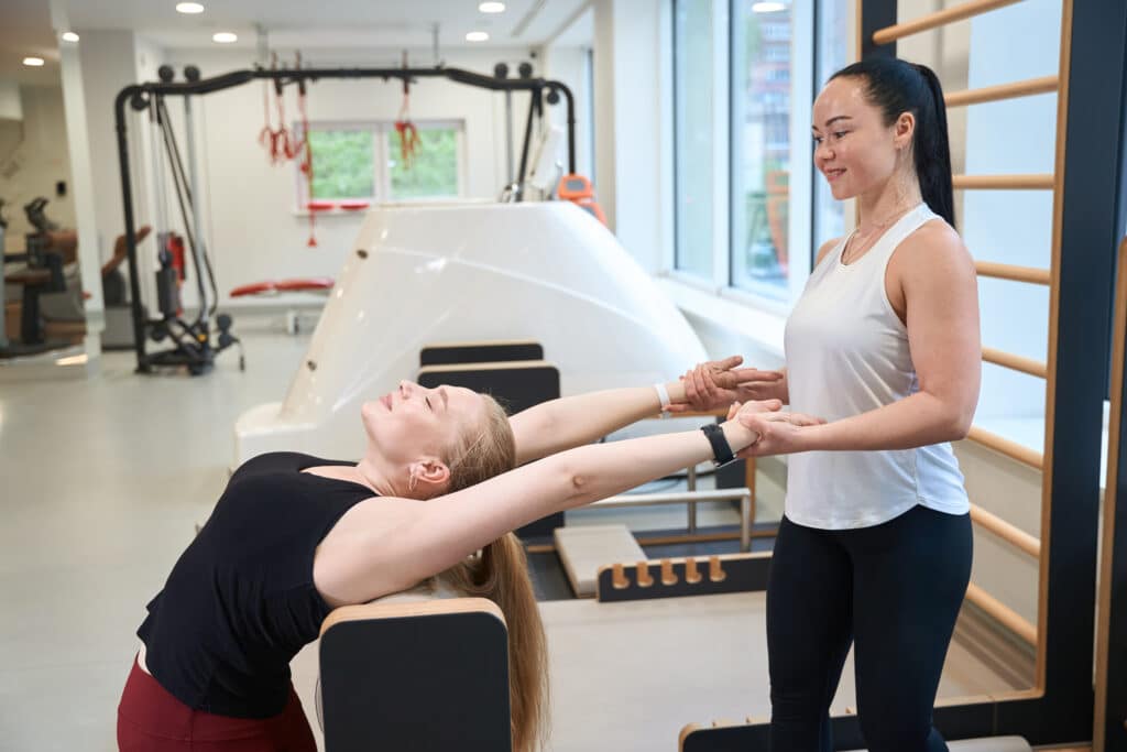 Blonde woman performs stretching exercises under the supervision of trainer Blonde woman performs stretching exercises under the supervision of trainer