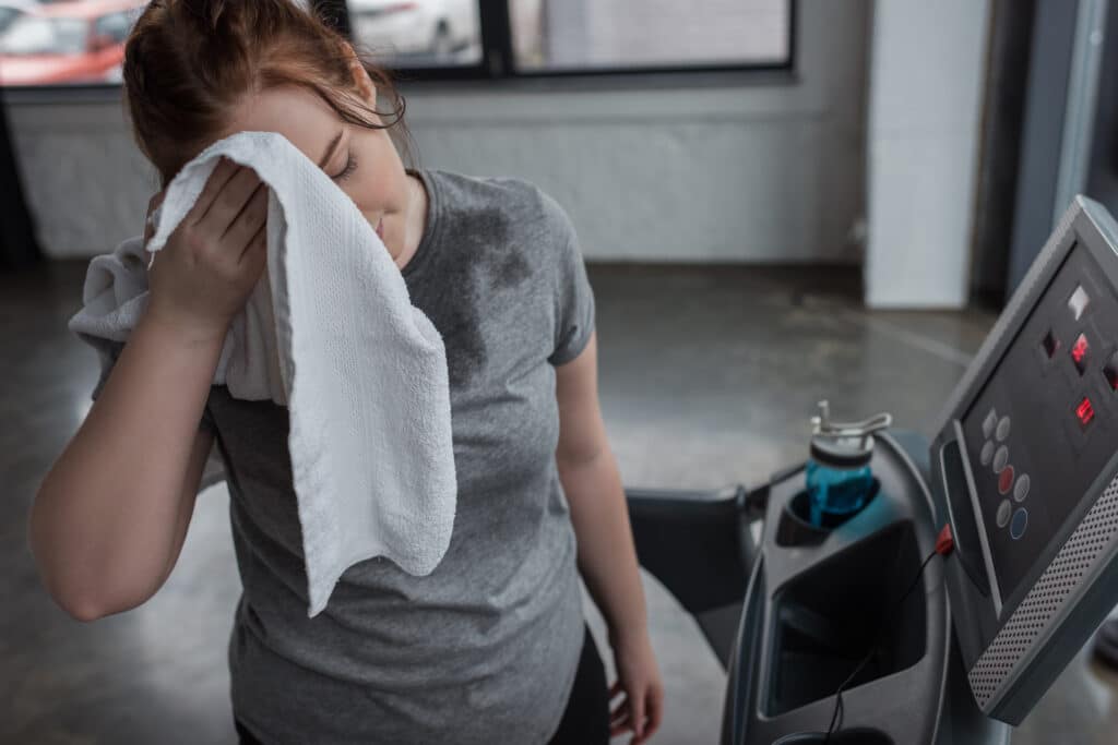 Obese girl wiping her face while running on treadmill in gym