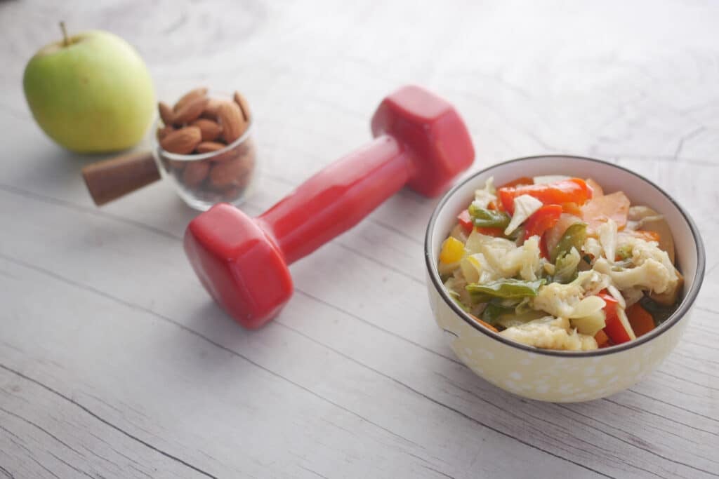 Fitness concept with dumbbell, fresh vegetable , almond and apple on table