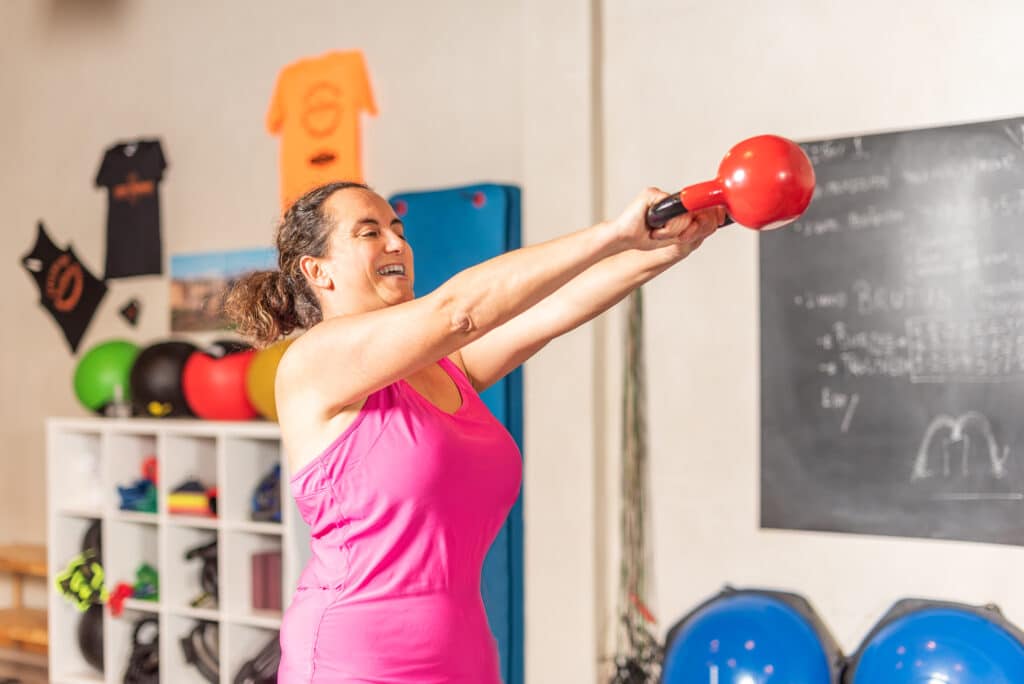 Woman doing kettlebell swing exercise in gym