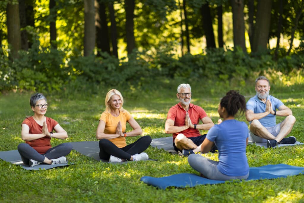 Group of senior people attending yoga class with instructor outdoors