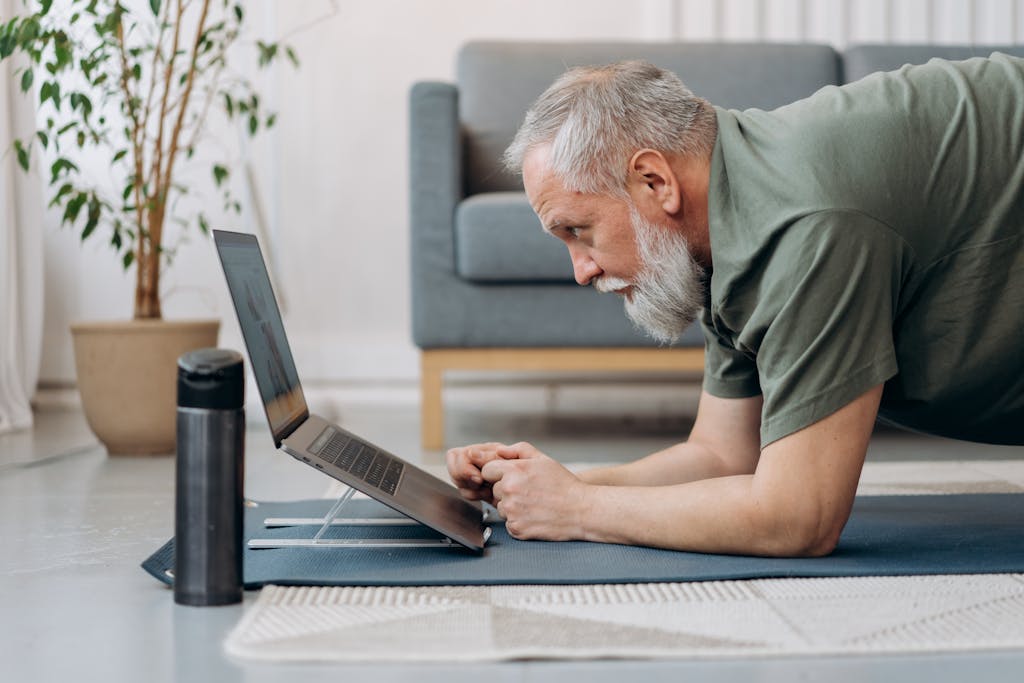 Photo by Mikhail Nilov An Elderly Man Working Out while Looking at the Laptop