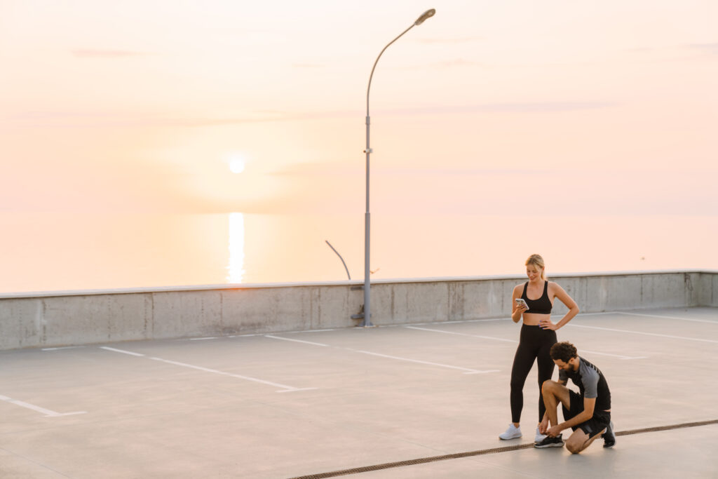 Young man and woman using cellphone while working out together on parking