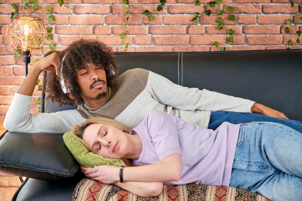 multiracial young couple lying on the sofa at home resting sleeping and listening to music