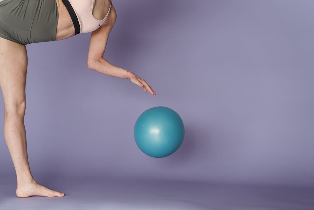 What to Wear to Pilates: A Complete Guide Side view of crop anonymous strong gymnast performing exercise with gym ball on purple background