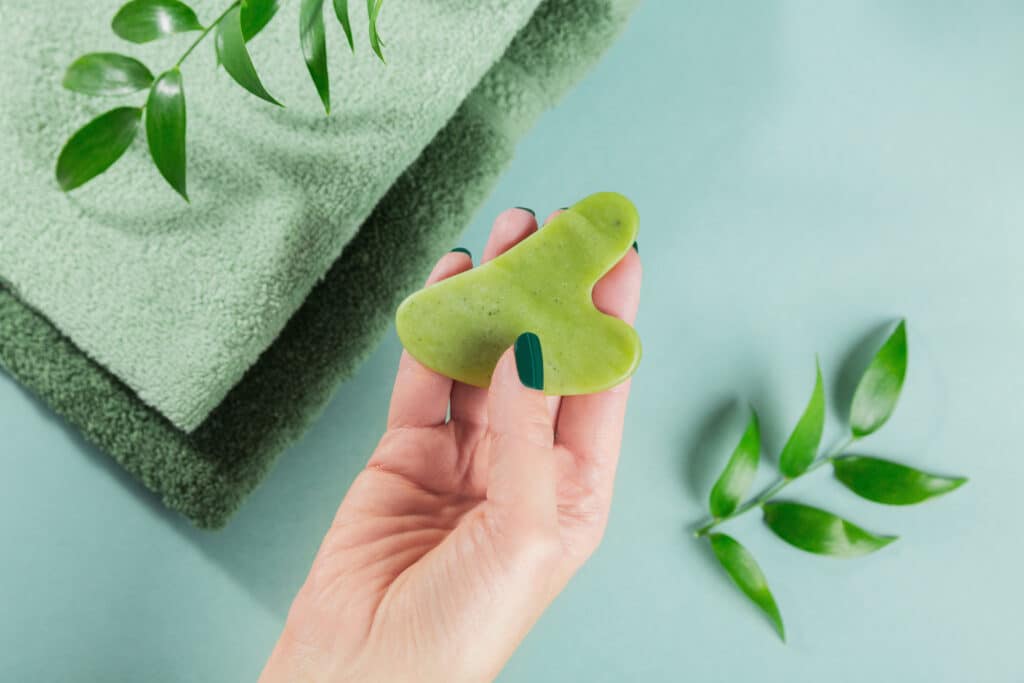 Female hand holding massage gua sha scraper for the face of green jade stone