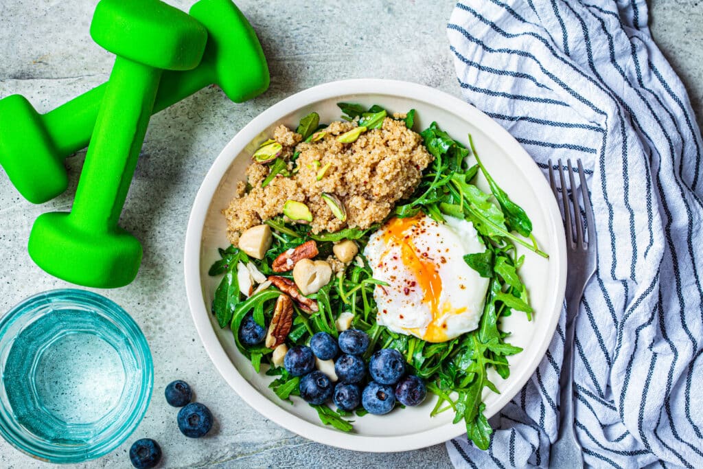 Quinoa salad with berries, poached egg and nuts, dumbbells on th