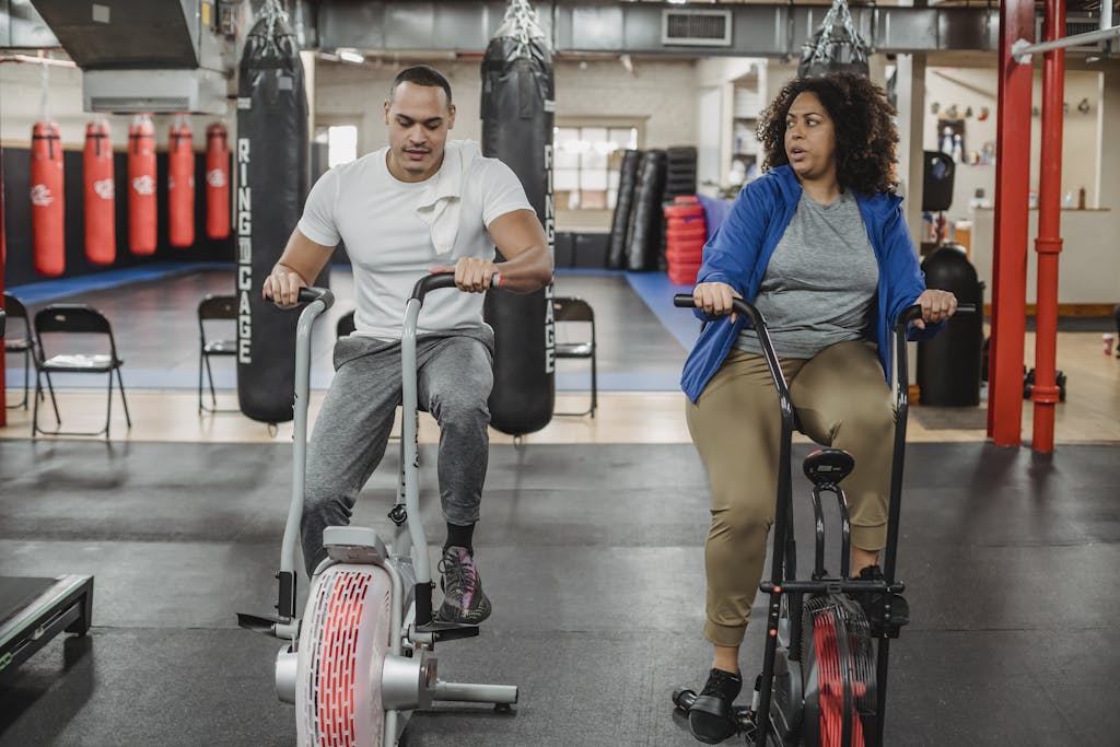 Tabata Ride: A High-Intensity Workout for Maximum Results Full body of overweight black woman sitting on cycling machine and looking at fitness trainer