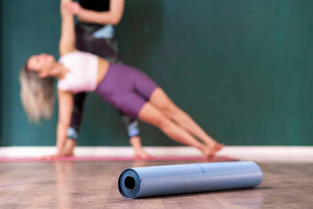 Gymnastic mat roll put on wooden floor against coach helping female student do exercise