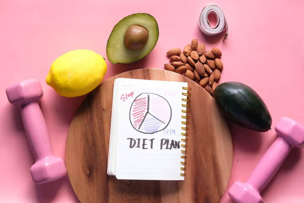handwritten diet plan on notepad with healthy fruits on pink background