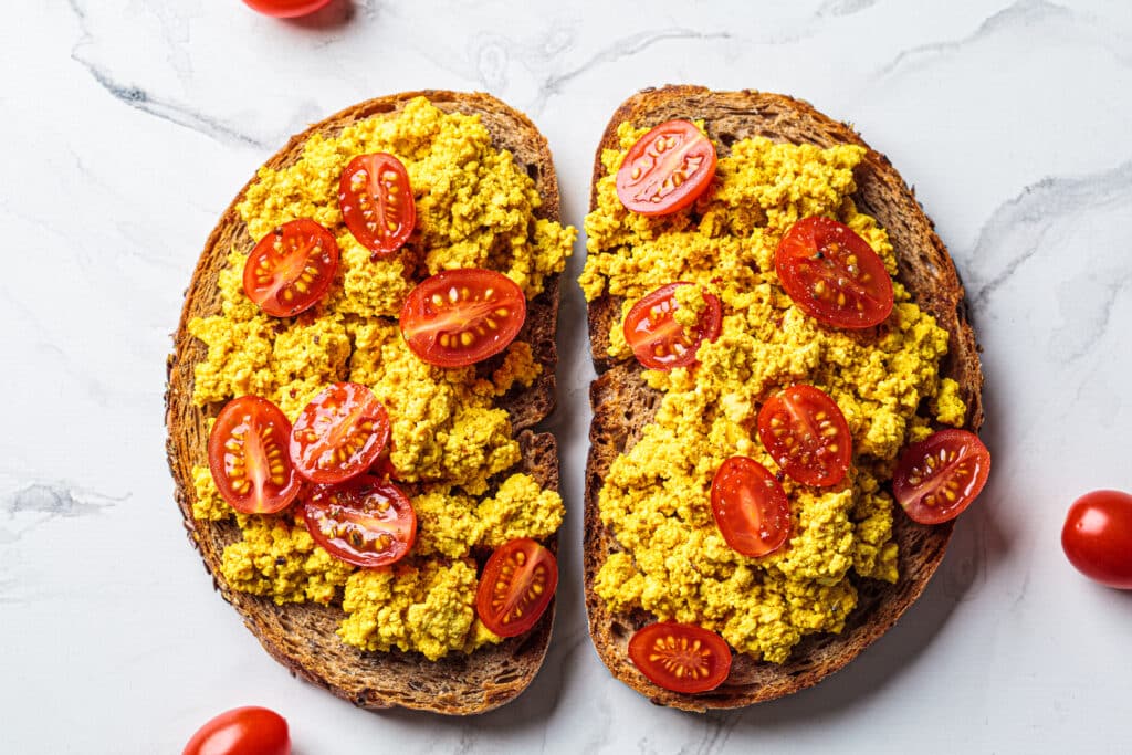 Tofu scrambled toast with tomatoes, white marble background. Pla