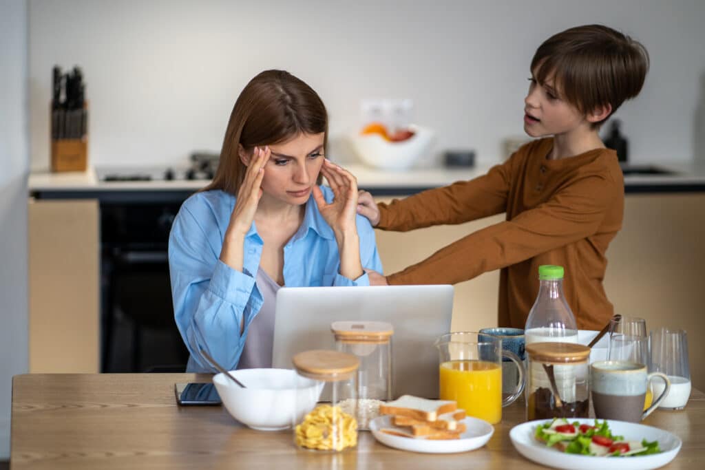 Small child worries mother working home sitting table in kitchen and having breakfast