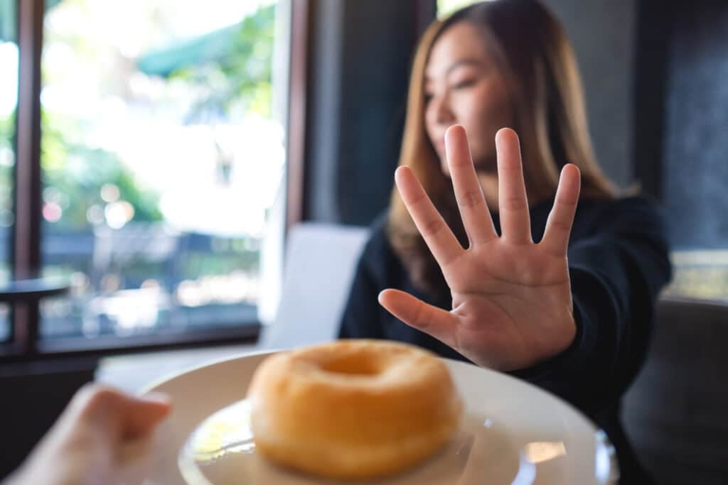 A woman making hand sign to refuse a donut from someone