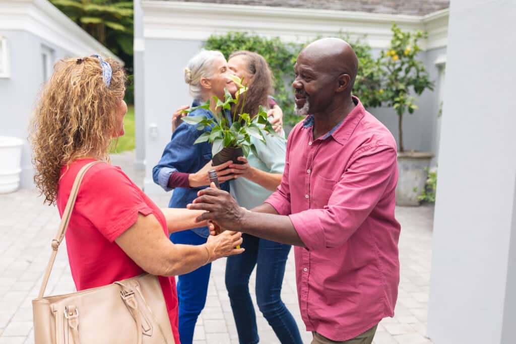 Senior man and woman welcoming multiracial friends at entrance during house party. unaltered, lifestyle, friendship, togetherness, party, leisure and social gathering.
