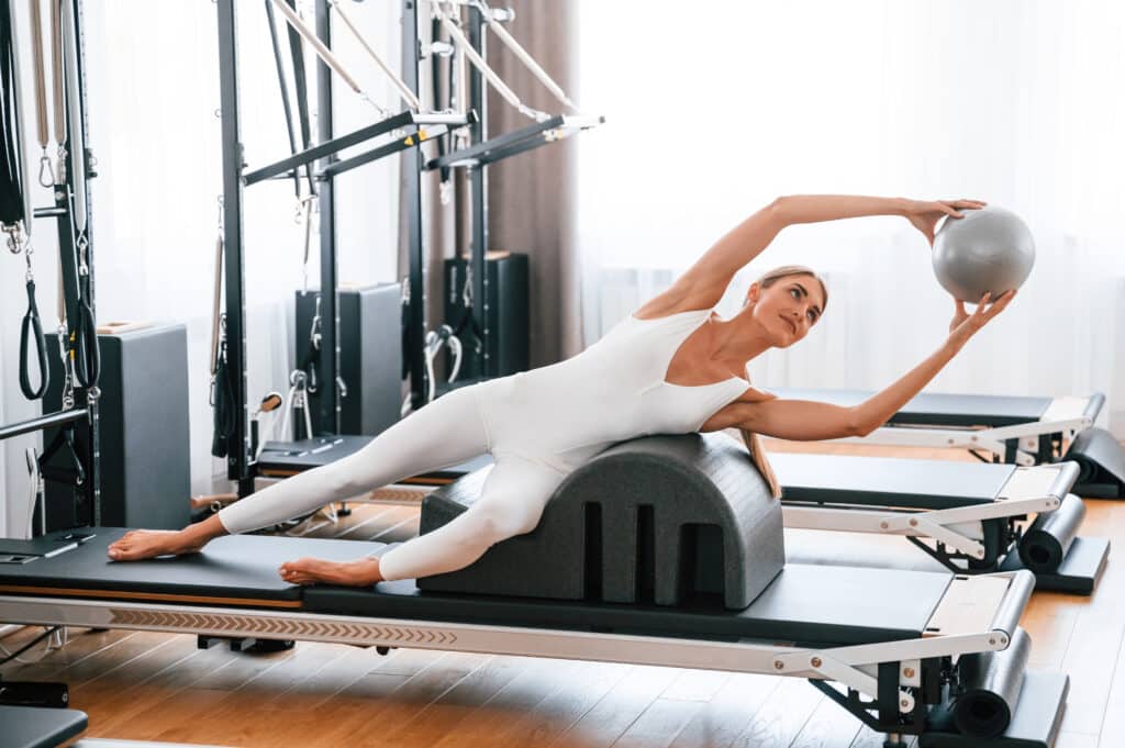 Holding ball in hands. Young woman in fitness center is doing exercises