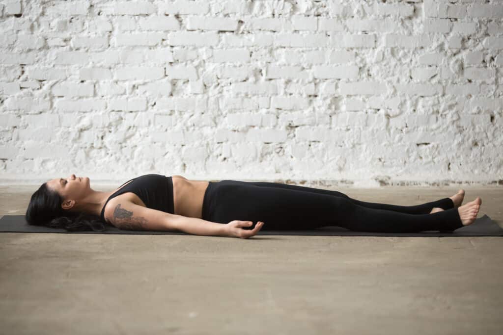 Young yogi attractive woman in Savasana pose, white loft backgro