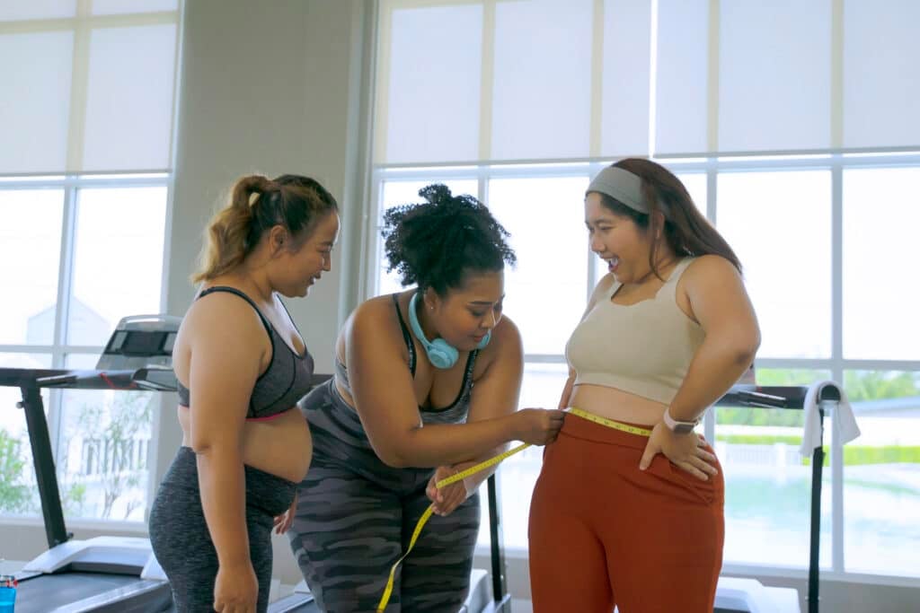 Plus size women measure their waist at fitness center. Plus size women measure their waist at fitness center.