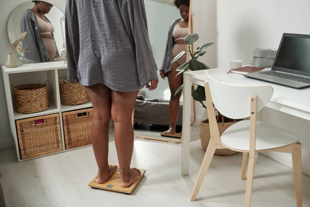 Young plus size woman in grey shirt standing on scales