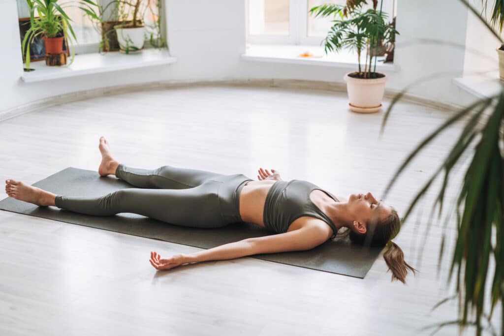 Young fit woman practice yoga doing savasana in light yoga studi