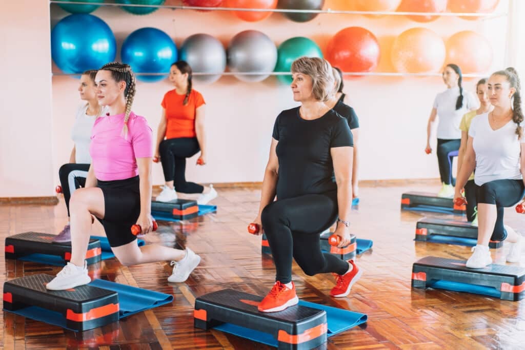 Group of women are engaged in step aerobics with dumbbells in their hands