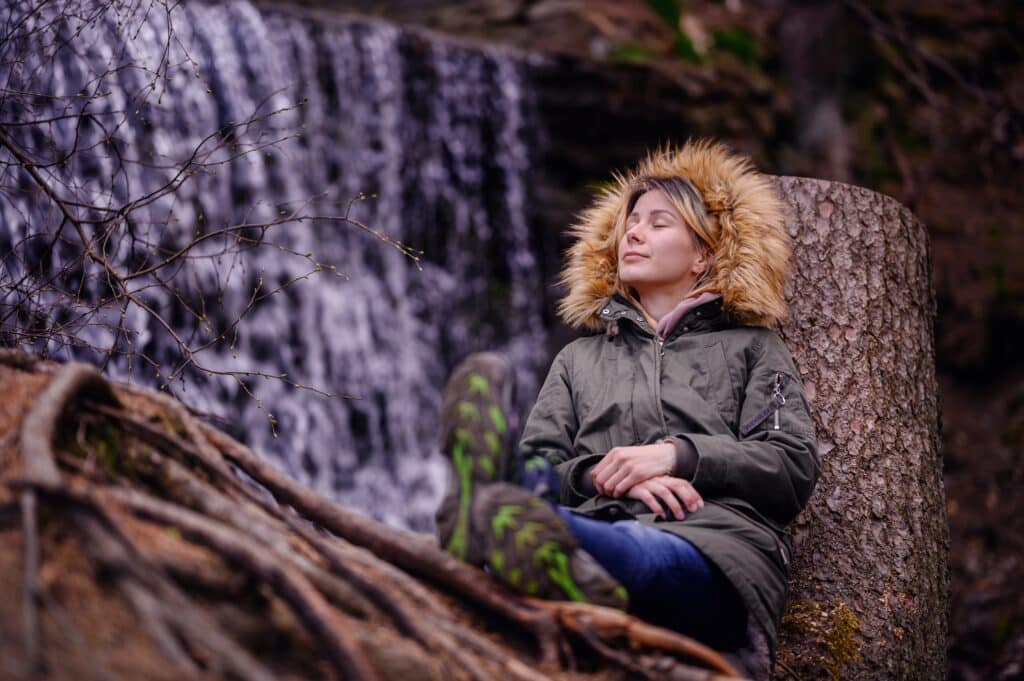 young-woman-sits-leaning-on-a-stump-in-green-parka-2023-11-27-05-18-31-utc