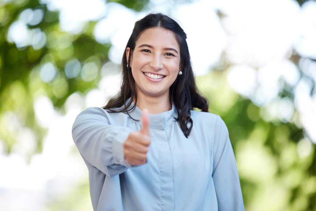 Portrait of a young businesswoman showing thumbs up in the city.