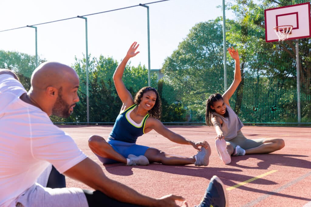 Happy biracial friends wearing sports clothes and warming up at basketball court. Sport, activity, friendship and lifestyle, unaltered.