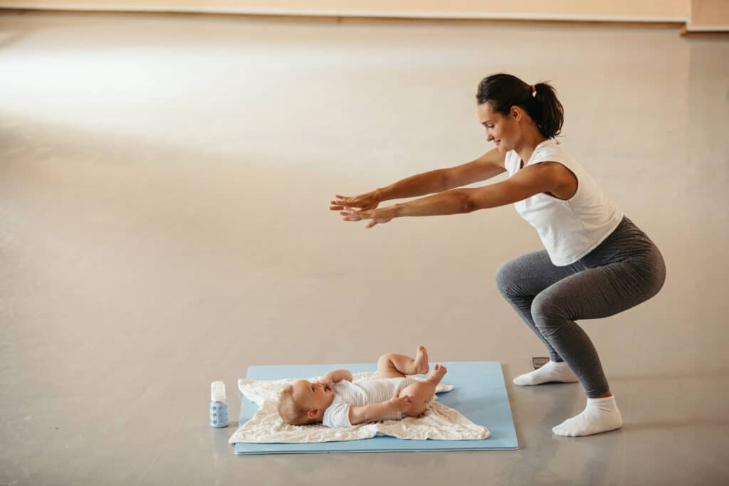 Athletic woman with baby doing squats on exercise class in health club.