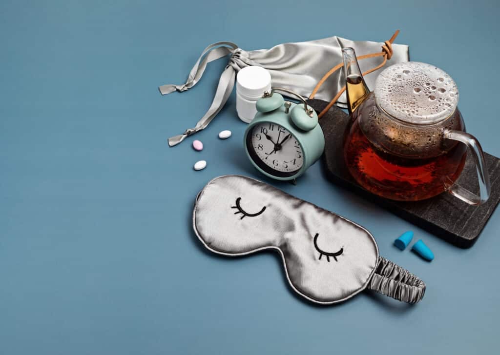 Classic alarm clock, sleeping mask, tea pot on blue pastel background. Minimal concept of rest, quality of sleep, good night, insomnia, relaxation