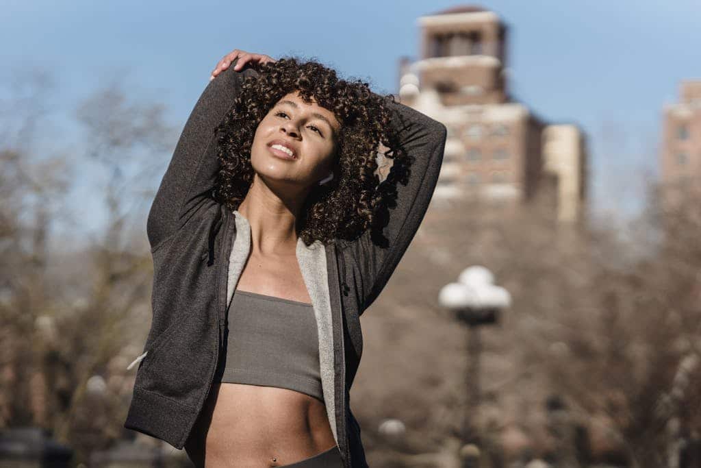 How to workout the right way: From Preparations to Recovery Sportive ethnic female in trendy sportswear stretching arms standing on street with trees and building on blurred background during workout