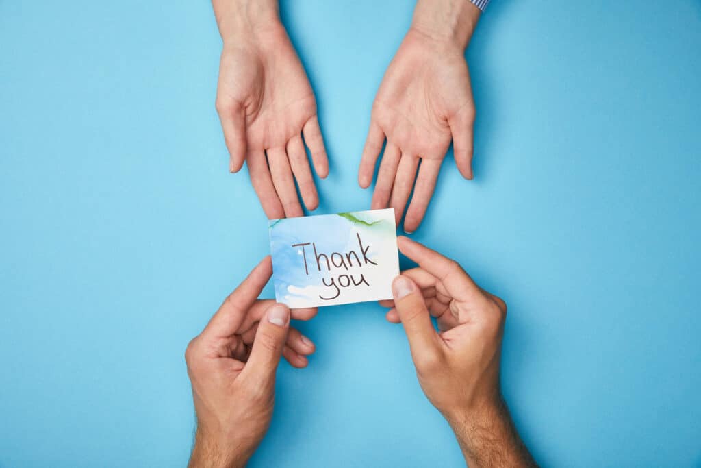 cropped view of man giving greeting card with thank you lettering to woman on blue background