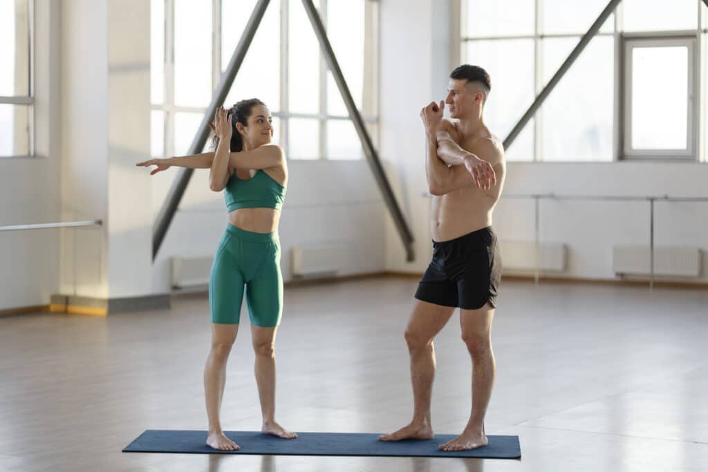 Smiling man and woman working out together, warming up before training, indoors in gym