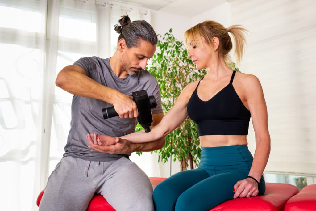 Concentrated Massage therapist using massage gun on client