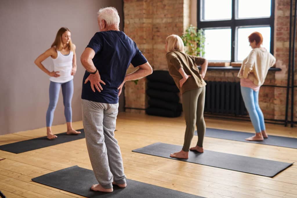 Young female trainer and group of senior people doing physical exercise