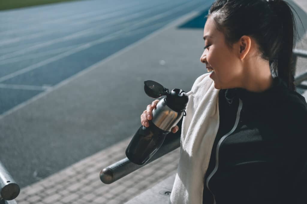 asian sportswoman with sport bottle and towel on running track on stadium