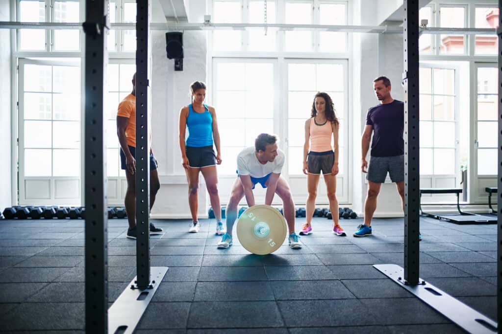 Young man lifting weights with friends watching in the background Young man lifting weights with friends watching in the background