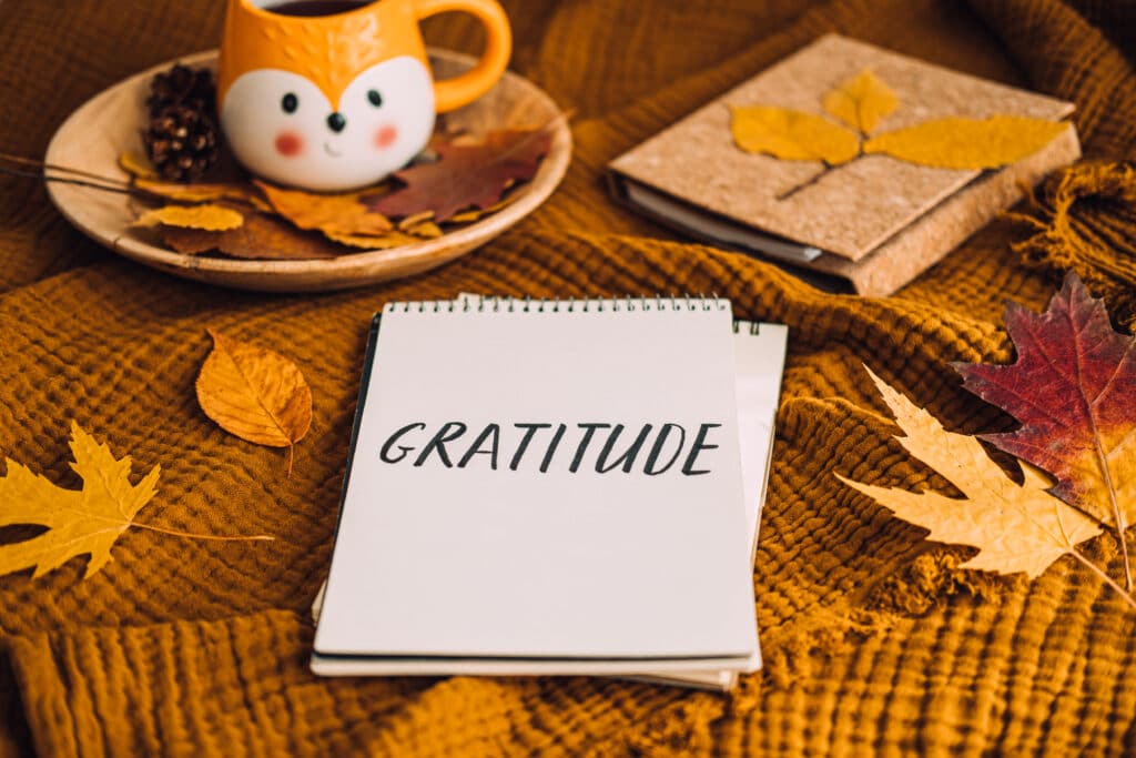 How to Practice Gratitude. Writing Autumn fall gratitude journal. Open paper notebook pages with Text gratitude and fall leaves brown bed. Notice appreciate good things, Express gratitude to yourself.