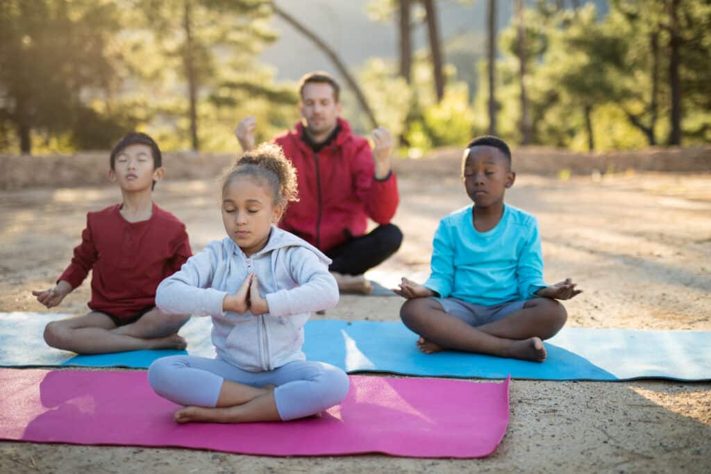 Coach and kids meditating in park on a sunny day