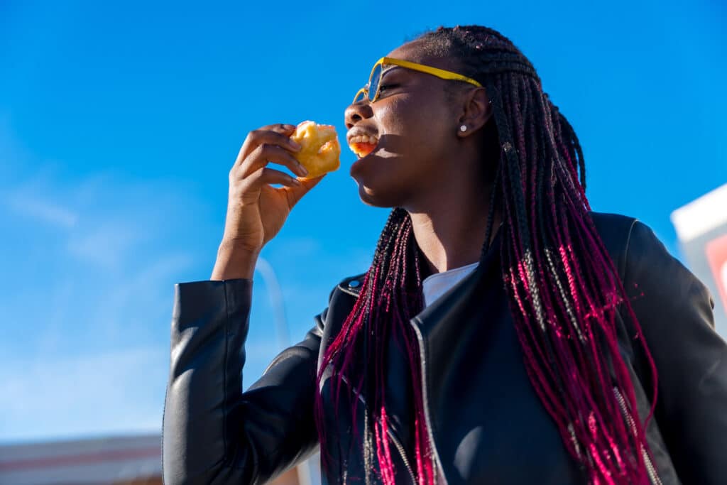 African woman enjoying the last piece of doughnut outdoors African woman enjoying the last piece of doughnut outdoors