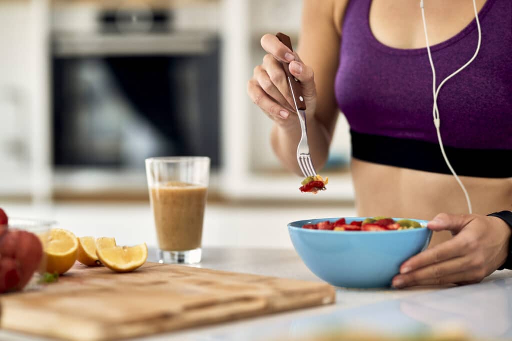 Close-up of athletic woman eating fruit salad in the kitchen.