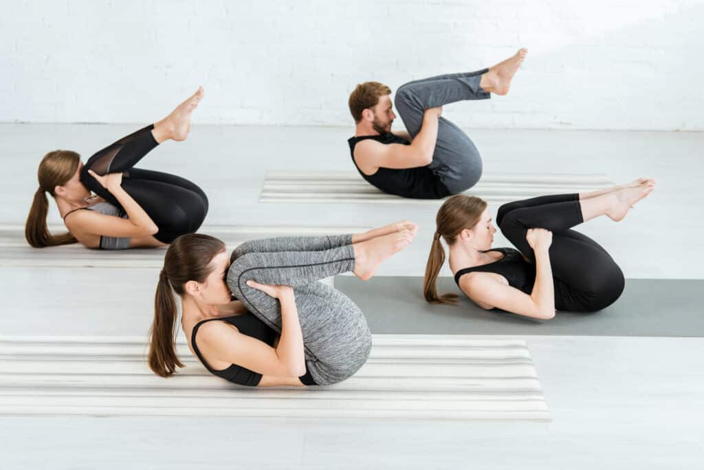 young people in sportswear practicing yoga in ball pose