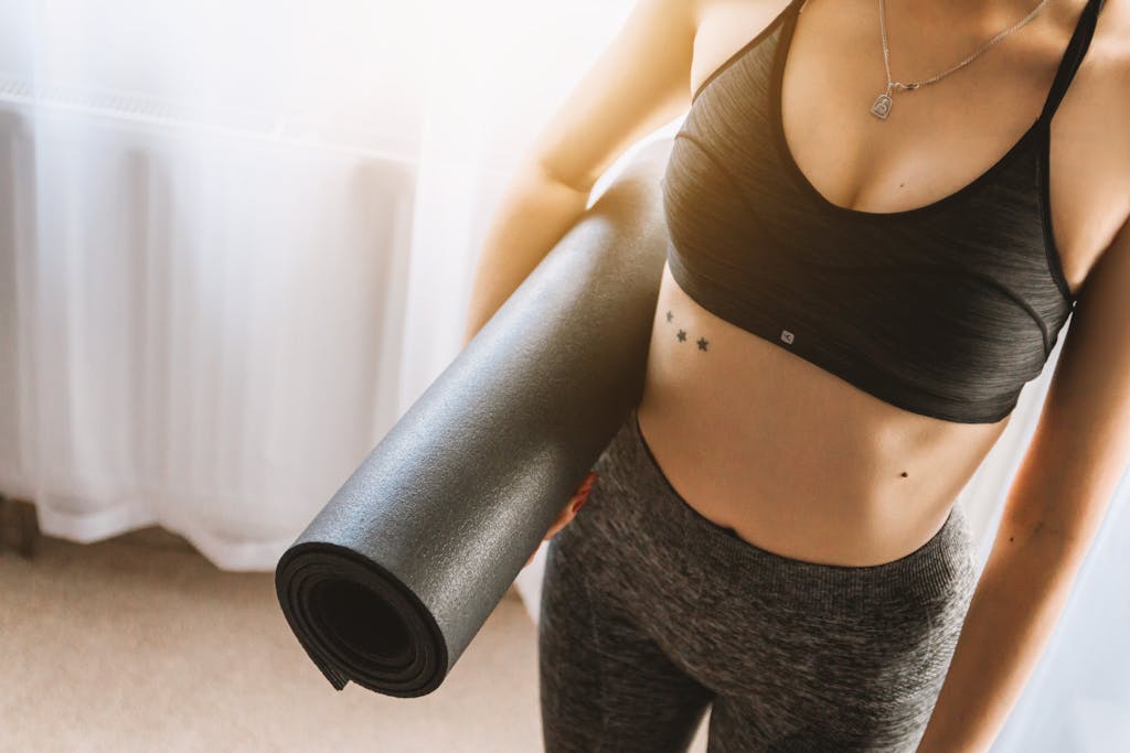 What to Wear to Pilates: A Complete Guide Woman in Black Sports Bra With Grey Leggings Carrying Yoga Mat