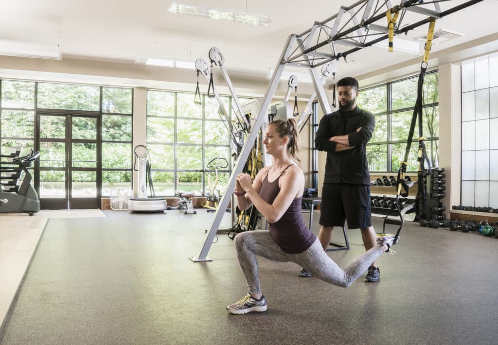 United States,Fitness coach watching woman using exercise machine at gym.