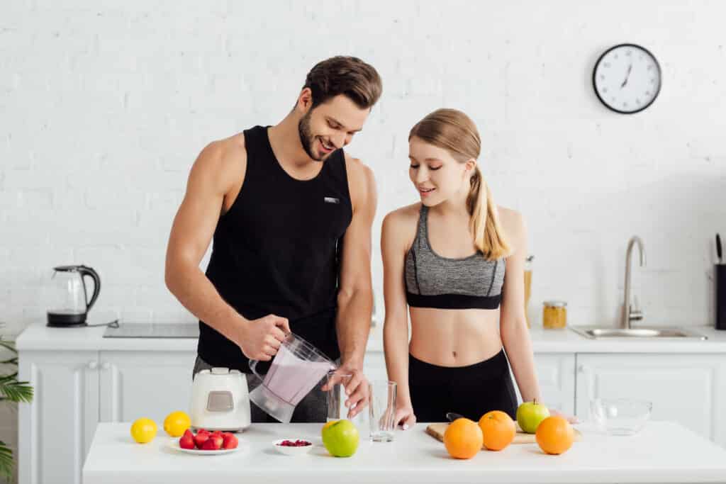 sportive man holding blender with smoothie near happy girl and fruits sportive man holding blender with smoothie near happy girl and fruits