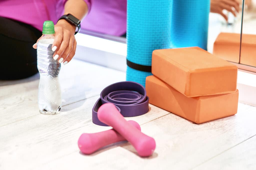 Fitness equipment. Dumbbells, yoga mat, resistance band and yoga bricks on wooden floor in studio