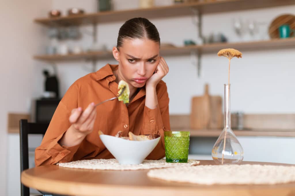 Taste trouble. Young caucasian woman showing dislike for her caesar salad, looking at it and dont want to eat