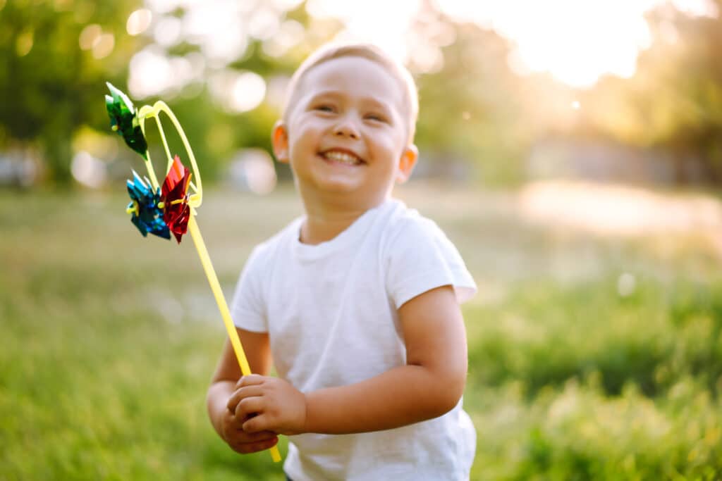 Smiling child with toy in summer park on sunny day. Cute little boy enjoying fresh spring weather.